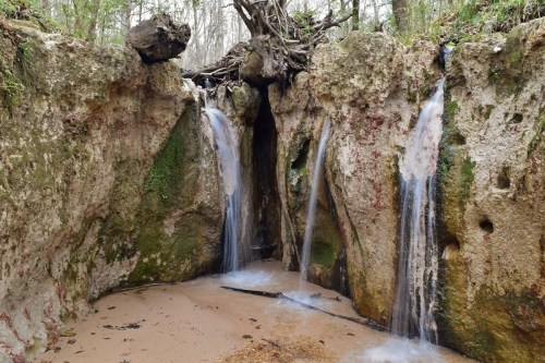 A serene scene of water cascading from rocky cliffs into a sandy area, surrounded by lush greenery.