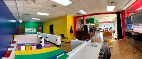 Brightly colored playroom with LEGO-like blocks, seating areas, and a kitchen visible in the background.
