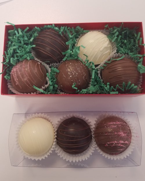 A red box containing six assorted chocolate truffles on green shredded paper, with two layers of treats.