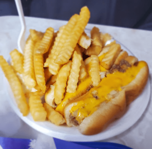 A plate of crinkle-cut fries next to a hot dog topped with melted cheese.