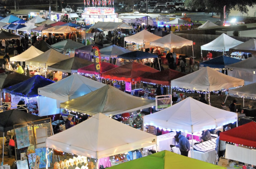 Aerial view of a vibrant night market with colorful tents and lights, bustling with visitors and various stalls.