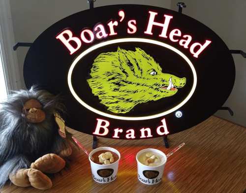 A Boar's Head sign with a plush boar and two cups of ice cream on a wooden surface.
