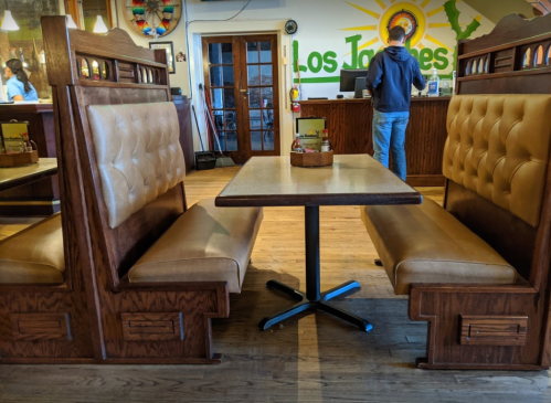 A cozy restaurant interior featuring wooden booths and a table, with a person standing at the counter in the background.