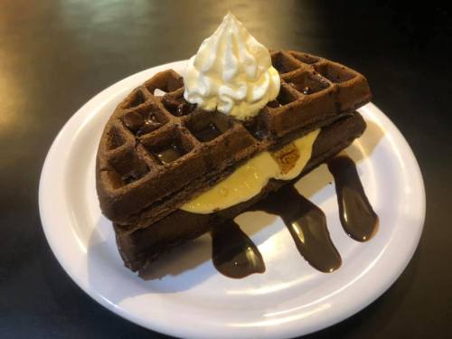 A chocolate waffle topped with whipped cream and drizzled with chocolate sauce, served on a white plate.