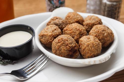 A plate of golden-brown fried meatballs served with a small bowl of dipping sauce.