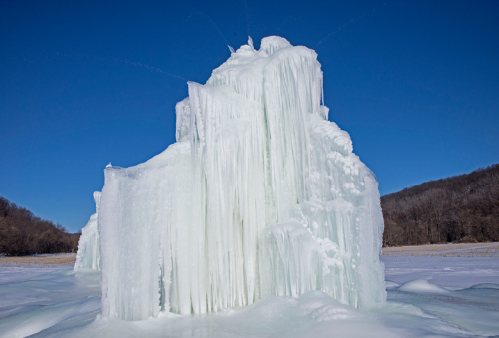 A tall, frozen ice formation with cascading icicles against a clear blue sky.