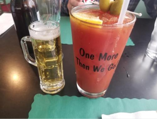 A tall glass of Bloody Mary with olives and lemon, next to a small mug of beer on a restaurant table.