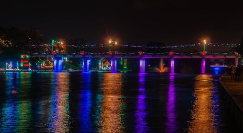 A brightly lit bridge adorned with colorful lights reflecting on the water at night.