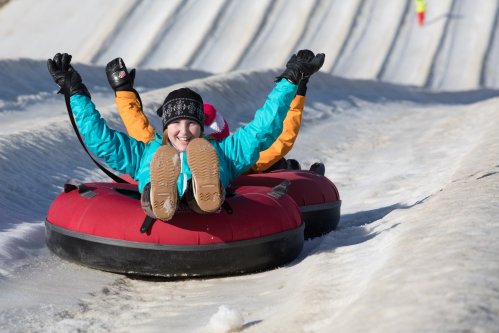 Two children joyfully tubing down a snowy slope, arms raised in excitement, wearing colorful winter jackets and gloves.