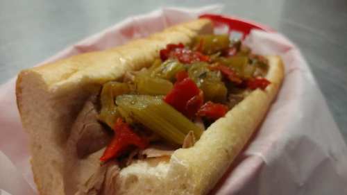 A sandwich filled with sliced roast beef, topped with green peppers and red peppers in a soft hoagie roll.