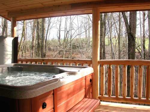 A wooden hot tub on a porch, surrounded by trees and a serene outdoor view.