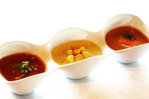 Three small bowls of colorful sauces: a red sauce, a yellow sauce with corn, and a brown sauce with a piece of meat.