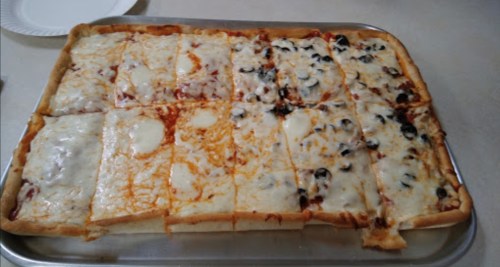A rectangular pizza with various toppings, including cheese, olives, and sauce, cut into square slices on a tray.