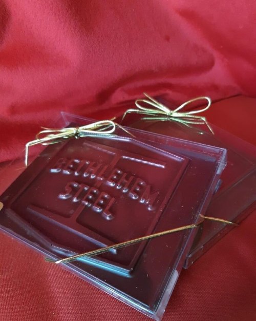Two clear coasters with "Bethlehem Steel" embossed, tied with gold ribbon, resting on a red fabric background.