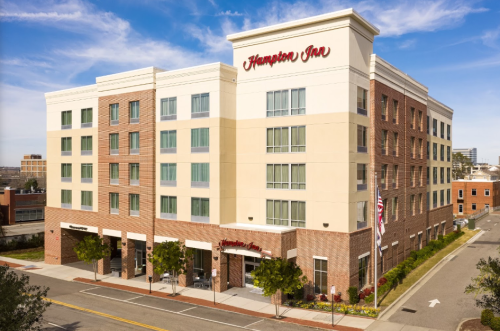 Exterior view of a Hampton Inn hotel, featuring a modern brick facade and clear blue sky.