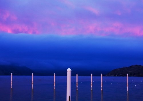 A serene lake at dusk, with white posts emerging from the water under a vibrant purple and blue sky.