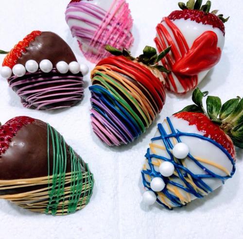 A variety of decorated strawberries, some dipped in chocolate and others in colorful icing, arranged on a white surface.