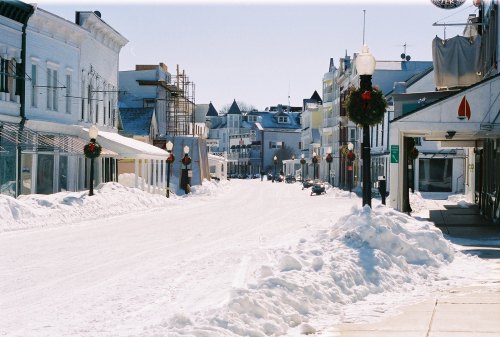 Snow-covered street lined with charming buildings and holiday decorations, under a clear blue sky.