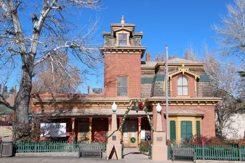 Historic brick building with festive decorations, surrounded by trees and a clear blue sky.