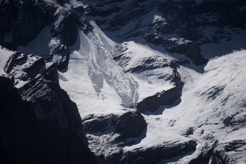 A snowy mountain landscape with a visible avalanche path and rugged terrain under a clear sky.