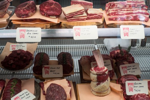 A display of various cuts of meat, including steaks and roasts, with price tags on a butcher shop counter.