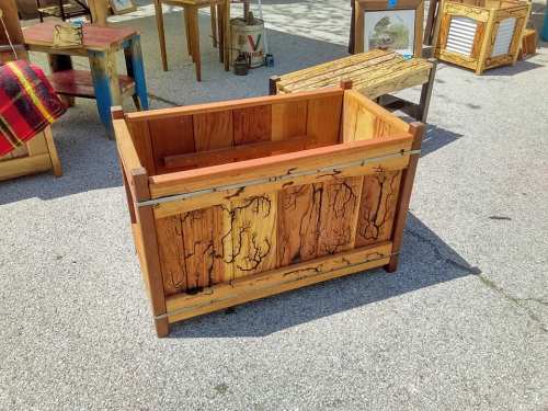 A rustic wooden planter box with a natural finish, featuring unique grain patterns, displayed outdoors among furniture.