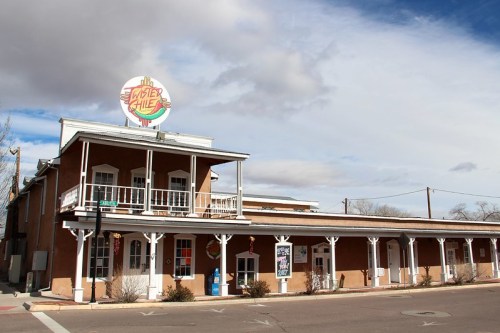 A southwestern-style building with a sign reading "Sister's Hill," featuring a balcony and cloudy sky above.