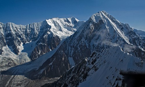 Snow-capped mountains under a clear blue sky, showcasing rugged peaks and a glacier in the valley below.