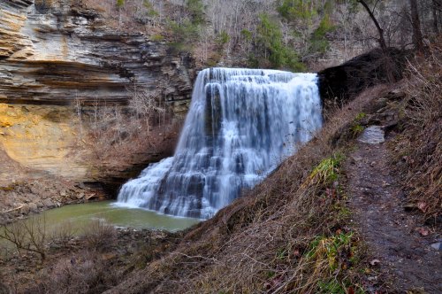 A cascading waterfall flows into a serene pool, surrounded by rocky cliffs and sparse vegetation.