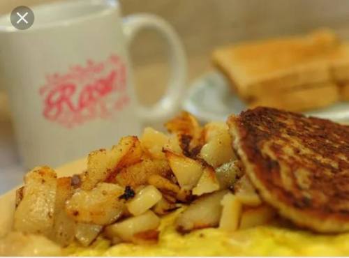 A close-up of a breakfast plate featuring an omelet, hash browns, and toast, with a coffee mug in the background.