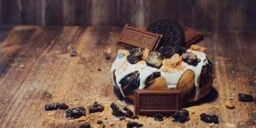 A decadent donut topped with chocolate frosting, crushed Oreos, and Hershey's chocolate bars on a wooden surface.