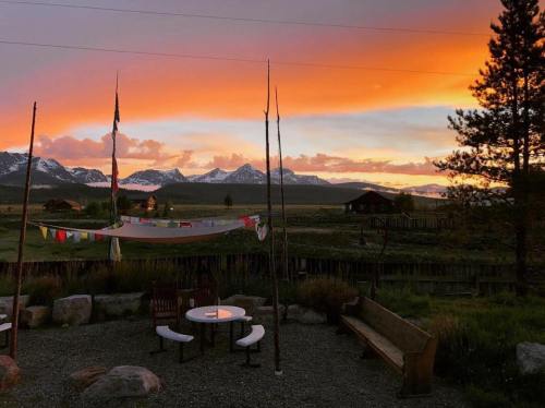 A serene landscape at sunset, featuring mountains, a hammock with prayer flags, and a cozy seating area.