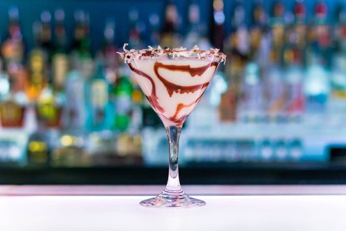 A decorative cocktail in a glass, featuring swirls of chocolate and cream, set against a blurred bar background.