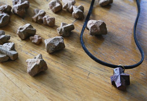 A black cord necklace with a star-shaped pendant next to scattered small stone pieces on a wooden surface.