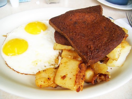 A plate with two sunny-side-up eggs, crispy potatoes, and two slices of dark toast.