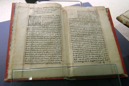Open antique book displaying text and illustrations on aged pages, resting on a display case.