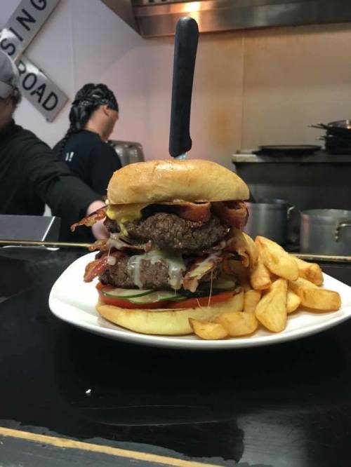 A large burger stacked with bacon, cheese, and toppings, served with golden fries on a plate.