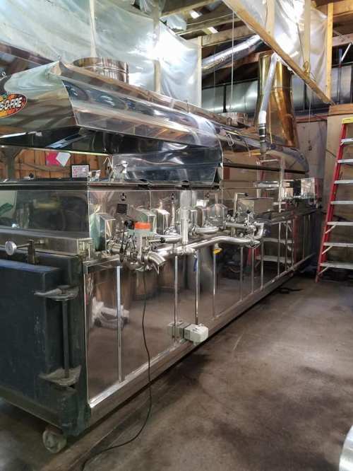 A large, shiny stainless steel syrup evaporator machine in a rustic workshop setting.