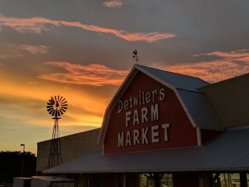 A farm market building with a windmill silhouette against a vibrant sunset sky.