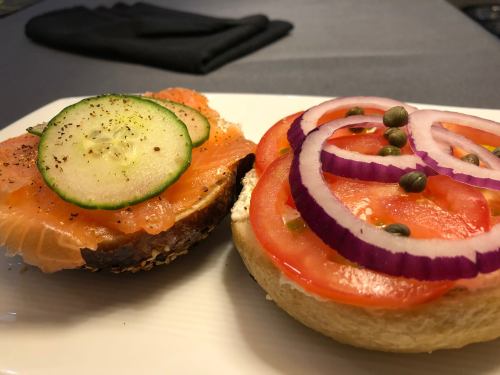 A plate with two open-faced sandwiches: one with smoked salmon, cucumber, and spices; the other with tomato, onion, and capers.