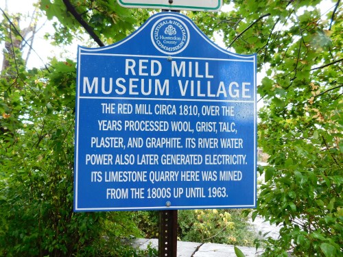 Sign for Red Mill Museum Village, detailing its history of processing materials and generating electricity.