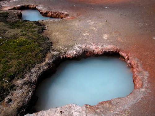 Two shallow, blue mineral pools surrounded by rocky, reddish terrain and patches of green moss.