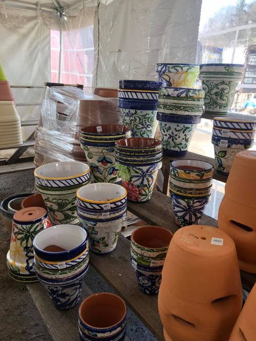 A variety of colorful ceramic and terracotta pots stacked on a wooden table inside a tent.