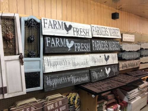 A display of decorative signs with phrases like "Farm Fresh," "Farmers Market," and "Happiness is Handmade" on wooden boards.