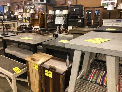 A furniture store display featuring various tables, chairs, and lamps, all with sale tags.