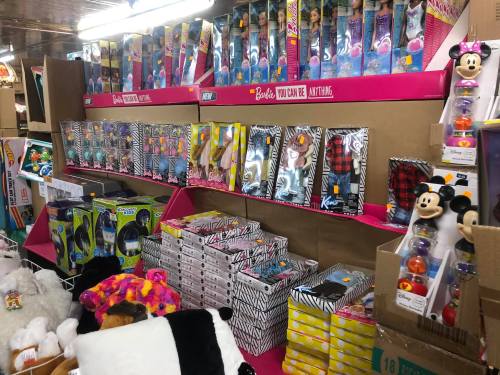 A colorful display of toys, including Barbie dolls, plush animals, and Disney figures, arranged on shelves in a store.