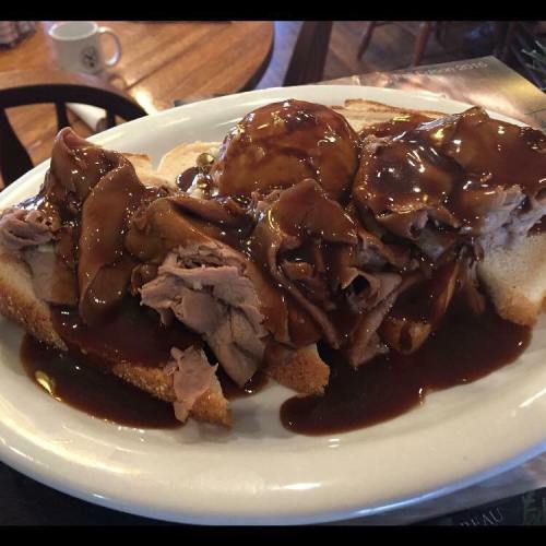 A plate of sliced roast beef on white bread, topped with gravy and served with a side of mashed potatoes.