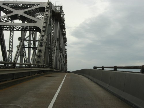 A view of a steel bridge with a cloudy sky, showing the road and structural details of the bridge.