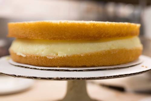 A two-layer cake with a creamy filling, resting on a cake stand in a kitchen setting.