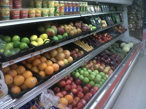 A grocery store display featuring a variety of colorful fruits, including apples, oranges, and grapes on shelves.